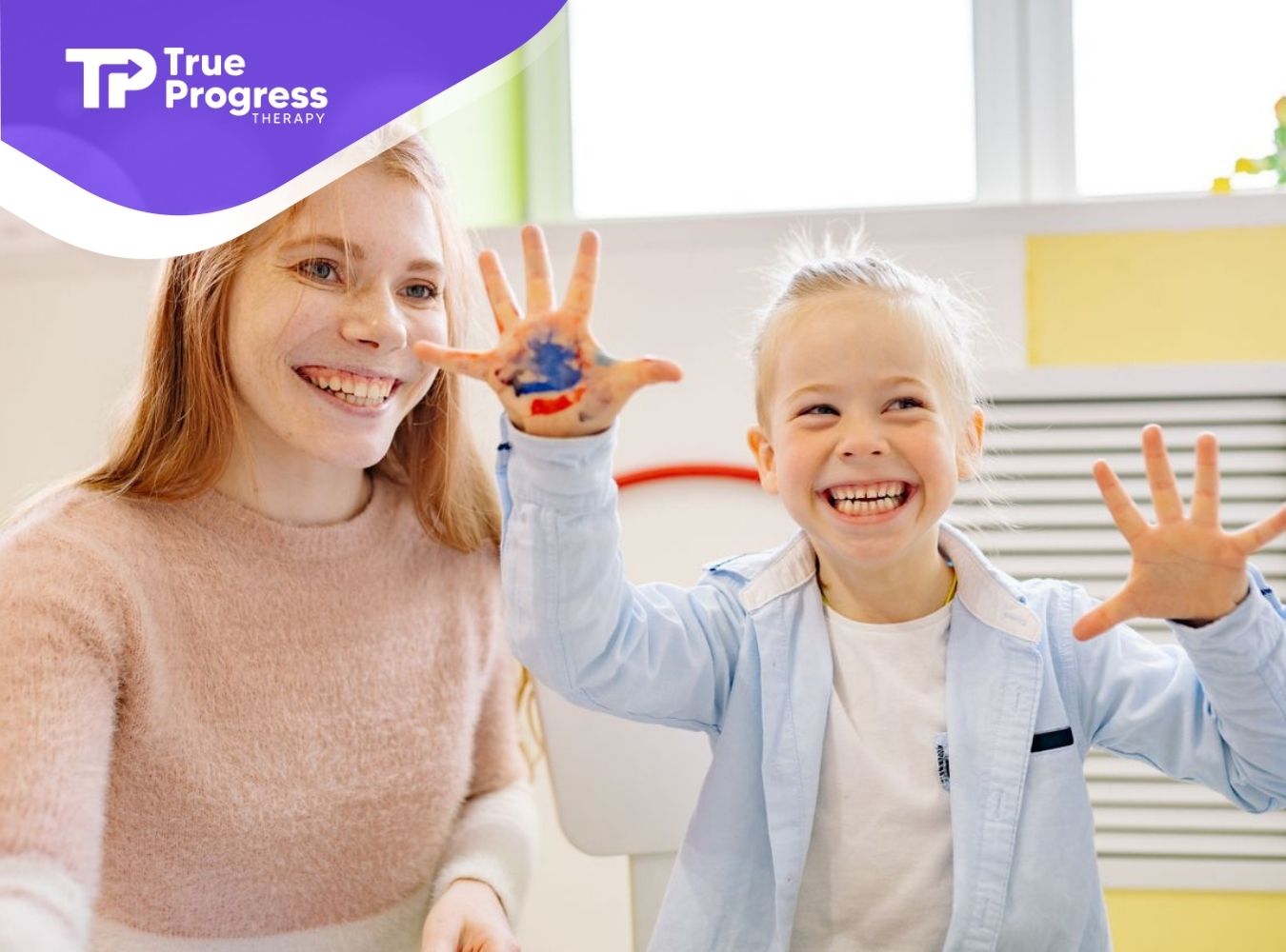 Smiling child showing painted hands during a creative, play-based ABA therapy activity with a therapist.